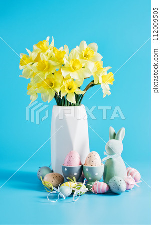 Happy Easter greeting card. soft pastel green Easter bunny figurine and collection of colorful, decorated Easter eggs against a vibrant blue background. Happy Easter greeting card. soft pastel green Easter bunny figurine and collection of colorful, decorated Easter eggs against a vibrant blue background. 112009505
