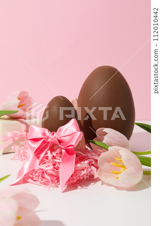 Chocolate egg with gifts and flowers on a light background 112010442
