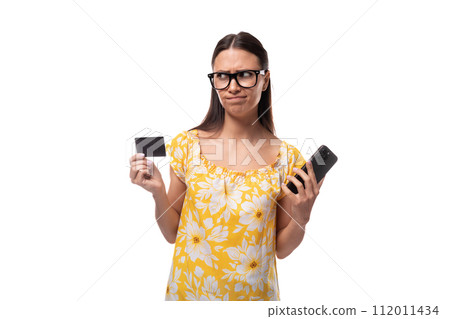 young brunette woman with straight hair dressed in a casual yellow T-shirt looks at the bank card young brunette woman with straight hair dressed in a casual yellow T-shirt looks at the bank card 112011434