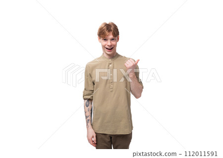 young red-haired man in a beige shirt points his finger to the side on a white background 112011591