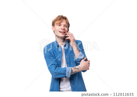portrait of a smiling caucasian red-haired guy in a denim blue shirt chatting on the phone 112011635