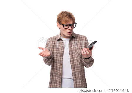 young caucasian red-haired guy in a shirt holding a smartphone at a loss 112011648