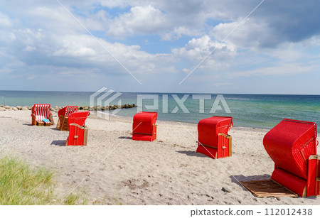 Traditional German roofed wicker beach chairs on the beach of Baltic Sea. Beach with red chairs on stormy sunny day. Ostsee. 112012438