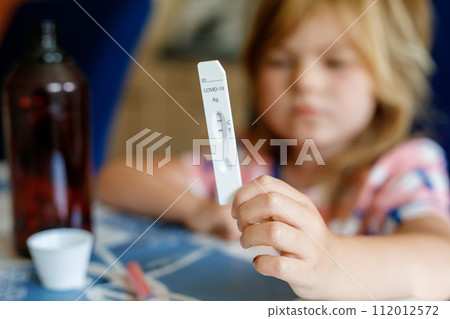Covid-19 testing children. Sad Child holding self rapid test with positive result. Coronavirus testing. Preschool girl 112012572
