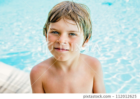 Portrait of happy little kid boy resting near the pool and having fun on family vacations in a hotel resort. Healthy child playing in water, swimming and splashing. 112012625