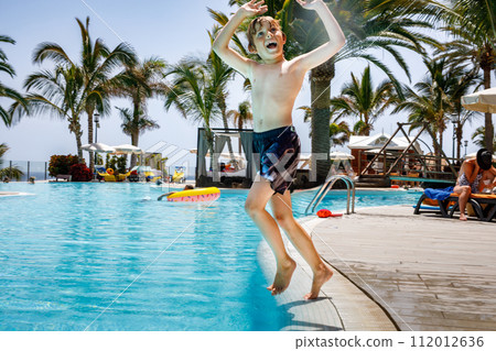Happy little kid boy jumping in the pool and having fun on family vacations in a hotel resort. Healthy child playing in water. 112012636