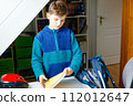 School kid boy getting ready in the morning for school. Healthy child filling satchel with books, pens, folders and school stuff. Preaparation, routine concept. 112012647