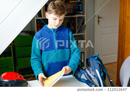School kid boy getting ready in the morning for school. Healthy child filling satchel with books, pens, folders and school stuff. Preaparation, routine concept. School kid boy getting ready in the morning for school. Healthy child filling satchel with books, pens, folders and school stuff. Preaparation, routine concept. 112012647