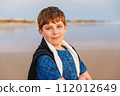 Happy cheerful teenager standing on beach at sunset. happy preteen boy smiling at the camera. Kid on family vacation at the sea. 112012649