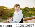 Happy cheerful teenager standing on beach at sunset. happy preteen boy smiling at the camera. Kid on family vacation at the sea. 112012657