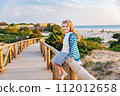 Adorable happy smiling little girl on beach vacation at sunset. Handsome cute preschool child with long blond hairs having fun on family vacations. 112012658