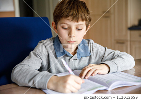 Upset school kid boy making homework during quarantine time from corona pandemic disease. Crying and sad boy frustrating staying at home. 112012659