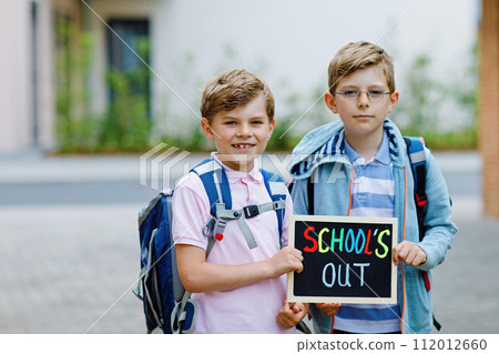 Two little kid boys with backpack or satchel. Schoolkids on the way to school. Healthy children, brothers and best friends outdoors on street leaving home. School's out on chalk desk. Happy siblings. 112012660