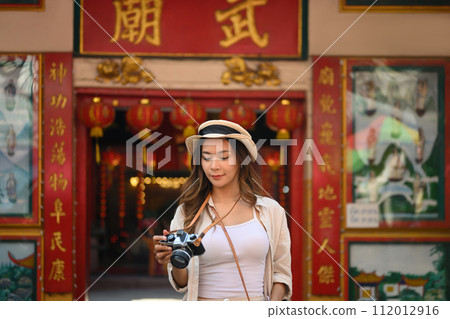 Beautiful female traveller with camera standing against a Chinese Temple located in Chang Mai Thailand 112012916