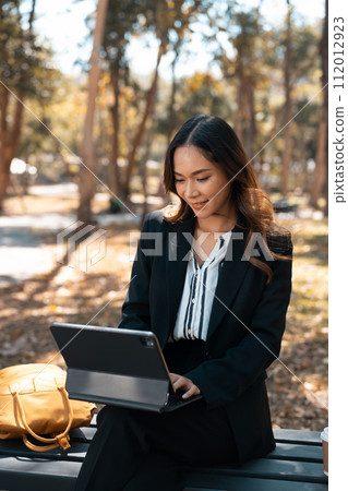 Portrait of attractive businesswoman sitting on a park bench and using digital tablet Portrait of attractive businesswoman sitting on a park bench and using digital tablet 112012923