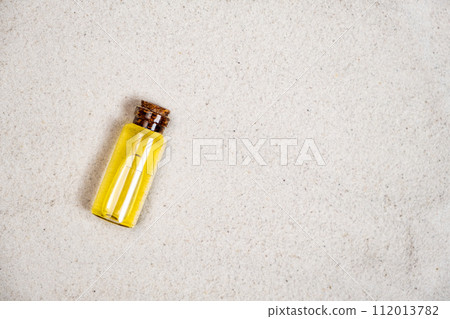 Essential oil in glass bottle on sand, top view, space for text. 112013782