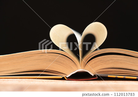 The pages of the book are folded in the shape of a heart on a black background, place for text The pages of the book are folded in the shape of a heart on a black background, place for text 112013783