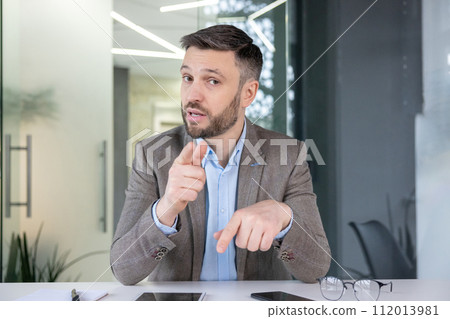 Professional male executive points and explains concepts during a corporate meeting in a modern office setting. Professional male executive points and explains concepts during a corporate meeting in a modern office setting. 112013981