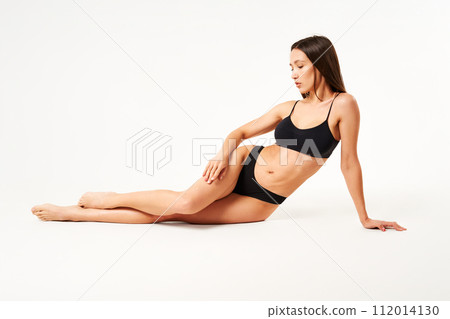 Young beautiful woman with perfect body in black underwear sitting on floor posing on studio 112014130