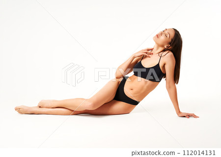 Young beautiful woman with perfect body in black underwear sitting on floor posing on studio 112014131