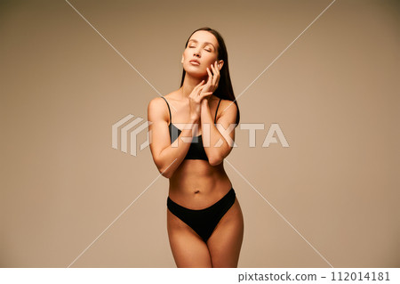 Sensual slim woman in black underwear posing on beige studio background Sensual slim woman in black underwear posing on beige studio background 112014181