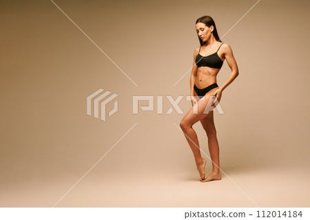 Pretty sporty woman in black underwear posing on beige studio background 112014184