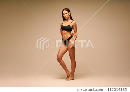 Pretty sporty woman in black underwear posing on beige studio background Pretty sporty woman in black underwear posing on beige studio background 112014185