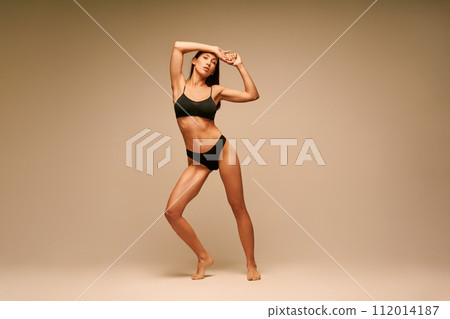 Pretty sporty woman in black underwear posing on beige studio background Pretty sporty woman in black underwear posing on beige studio background 112014187