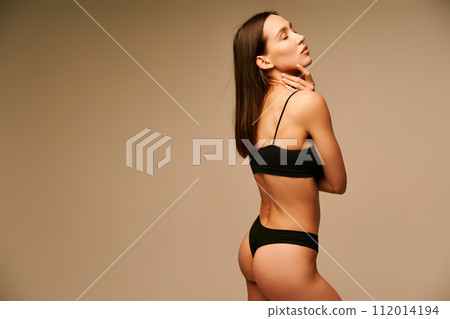 Beautiful sporty woman in black underwear posing on beige studio background 112014194