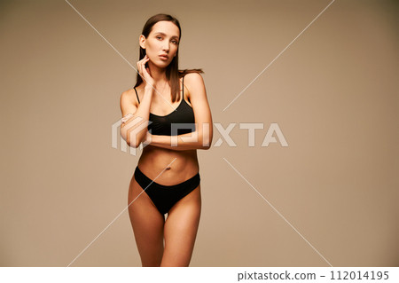 Beautiful sporty woman in black underwear posing on beige studio background Beautiful sporty woman in black underwear posing on beige studio background 112014195