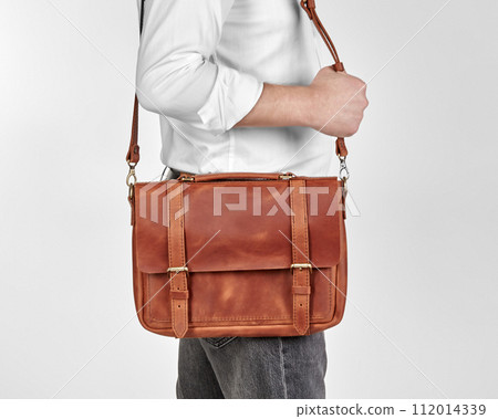 Man carrying copper-colored leather messenger bag over shoulder Man carrying copper-colored leather messenger bag over shoulder 112014339