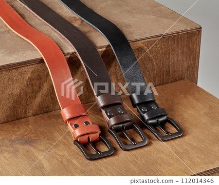 Three leather belts of different colors displayed on wooden stand 112014346