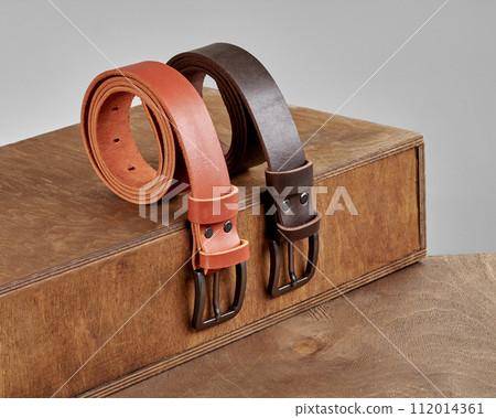 Two leather belts with embossment showcased on wooden display steps 112014361