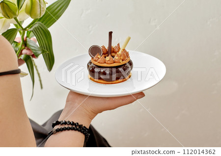 Exquisite chocolate mousse cake with caramel and gold flakes in female hand 112014362