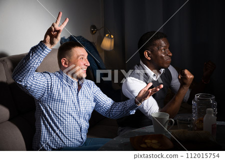 Positive male interracial friends watching football match on tv Positive male interracial friends watching football match on tv 112015754
