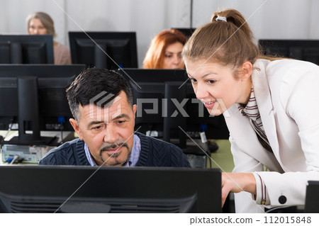 Woman explaining something to man coworker, pointing at computer monitor Woman explaining something to man coworker, pointing at computer monitor 112015848