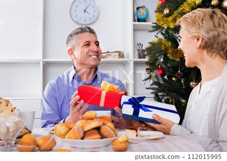 Mature couple gives gifts to each other for Christmas for festive table 112015995