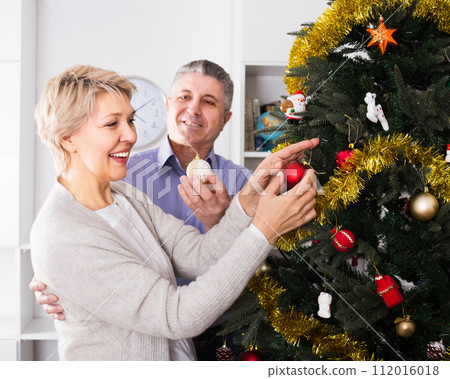 Woman and man are hang up New Year's toys on a fir-tree Woman and man are hang up New Year's toys on a fir-tree 112016018