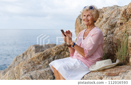 Elderly woman using phone at seaside Elderly woman using phone at seaside 112016593