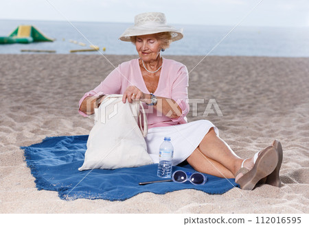 Elderly woman relaxing on beach Elderly woman relaxing on beach 112016595