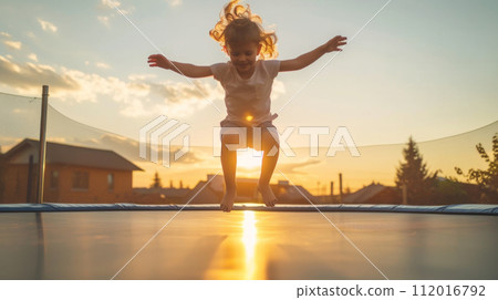 Child Jumping on Trampoline at Sunset 112016792