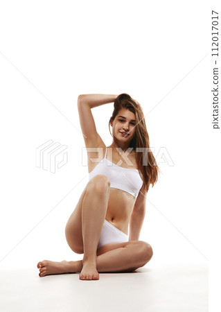 Beautiful young woman with slim fit body sitting on floor in comfortable cotton underwear against white studio background Beautiful young woman with slim fit body sitting on floor in comfortable cotton underwear against white studio background 112017017