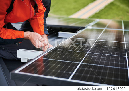Man technician mounting photovoltaic solar panels on roof of house. Close up view of engineer installing solar module system with help of hex key. Concept of alternative, renewable energy. Man technician mounting photovoltaic solar panels on roof of house. Close up view of engineer installing solar module system with help of hex key. Concept of alternative, renewable energy. 112017921