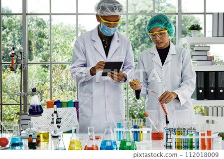 Two Lab scientists engaged and mix sample liqud in research and record result with digital tablet 112018009