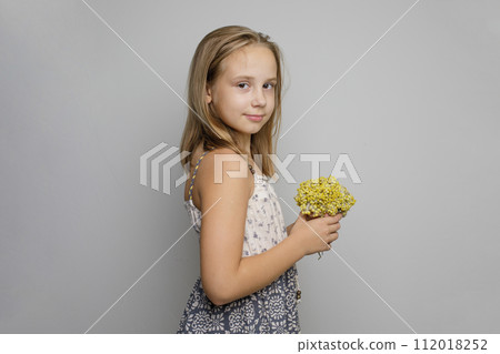 Beautiful young child girl wearing summer dress holding yellow flower standing Beautiful young child girl wearing summer dress holding yellow flower standing 112018252