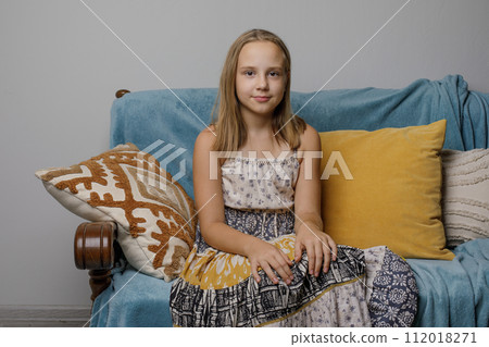 Cheerful child girl in summer dress relaxing on the sofa at home. 112018271