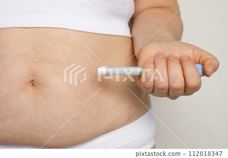 Woman hand holding self injection pen near her stomach. Medicine and treatment concept 112018347