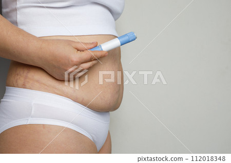 Female hand showing self injection pen near her stomach. Medicine and treatment concept 112018348