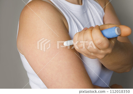 Female model making self injection with blue injection pen closeup. Medicine and treatment concept Female model making self injection with blue injection pen closeup. Medicine and treatment concept 112018350