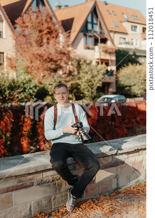 Man Sitting in Old European City And Holding Photo Camera. Contemporary Stylish Blogger And Photographer. Handsome man taking a selfie on a trip in Europe. 112018451